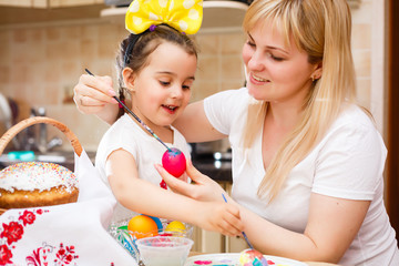 little girl painting easter eggs with mother