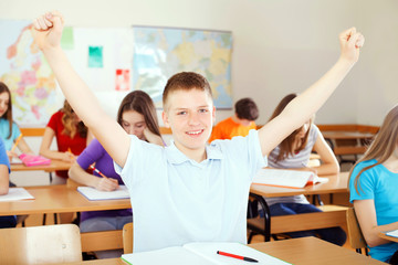 Happy pupil in classroom raising hands up.