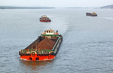 Large cargo barges transporting iron ore mined in hinterland to the main harbor for loading into...