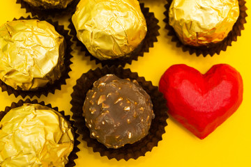Chocolate sweets with nuts in a golden wrapper on a yellow background with a red heart.