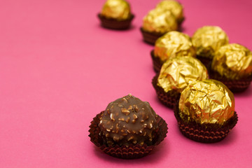 Chocolate sweets with nuts in a golden wrapper on a pink background, space for text.