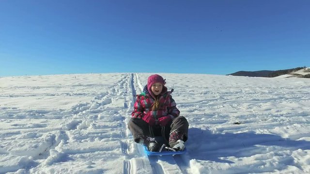 Little girl descending hill sledge on snowly hill