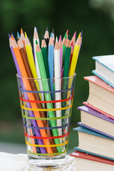Fototapeta premium Heap of colored pencils in a glass, books.