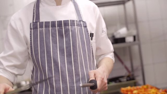Slow motion chef sharpens a professional steel knife close-up, standing in the kitchen of a cafe restaurant