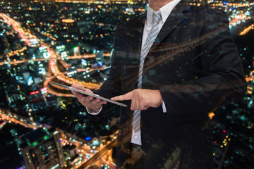 double exposure of business man using tablet with night modern city building background