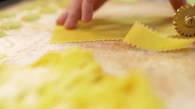 Close-up of men's hands use a professional roller knife to cut pasta from a piece of dough, on a table, sprinkled with flour, slow mo