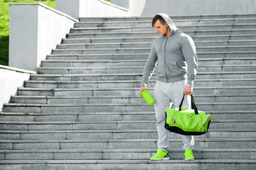 Active muscular man holding shaker and sports bag, outdoors.