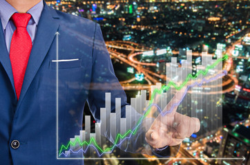 businessman point on virtual graph on screen with night modern city building background