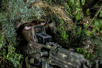 Camouflaged soldier aims his weapon