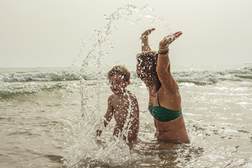 Woman and baby boy playing in the seashore of the beach. Summertime.