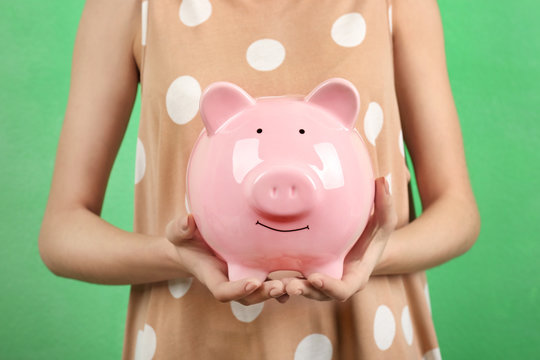 Young woman with piggy bank on color background, closeup