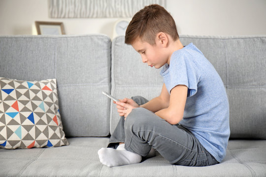 Incorrect posture concept. Schoolboy with phone sitting on sofa