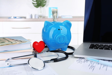 Piggy bank with little red heart and stethoscope on table