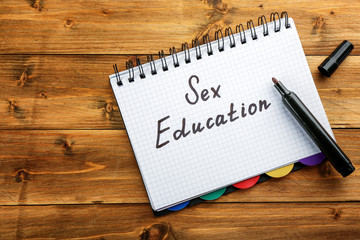 Exercise book with text SEX EDUCATION on wooden background
