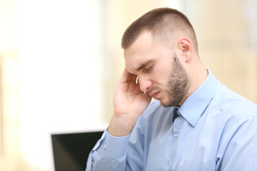 Fototapeta premium Handsome young man suffering from headache while working in office