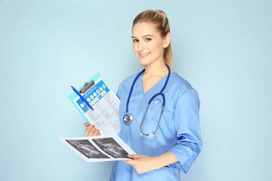 Young medical assistant with clipboard and sonogram image on color background