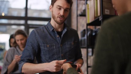  Customer in cafe makes payment with credit card while queue of customers wait