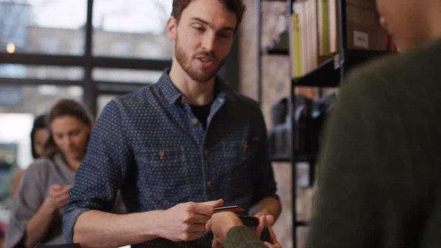  Customer in cafe makes payment with credit card while queue of customers wait