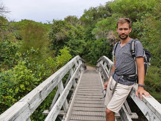 Male hiker with backpack standing on wood bridge on hiking track abel tasman track new zealand