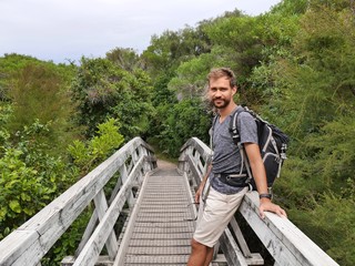 Male hiker with backpack standing on wood bridge on hiking track abel tasman track new zealand