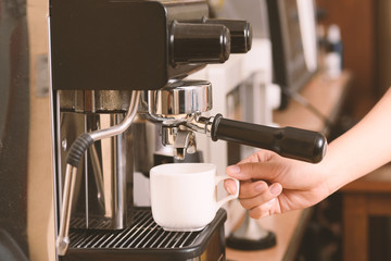 Barista holding white cup and making coffee from espresso machine