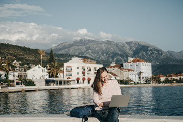 Young woman sitting on Embankment on the beach at sunset and prints in the laptop. Vacations,...