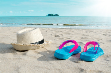 Straw hat and colorful flip flops on beach against sunny sky.