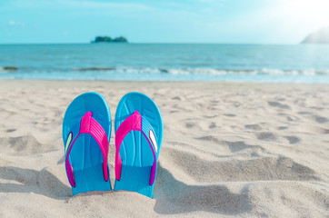 Colorful flip flops on beach against sunny sky.