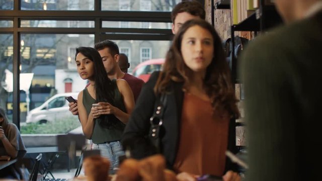  Queue of customers looking at mobile phones while they wait to be served in c