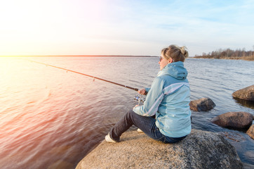 Girl sitting on a rock with a fishing rod - 144579126