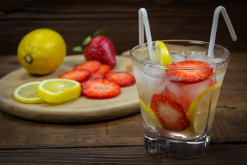 A refreshing summer drink with ice, strawberries and lemon on a wooden background. The concept of eating vegetarians, fresh vitamins, a homemade refreshing fruit drink.