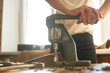 Female tailor working on vintage tools pressing buttons onto leather