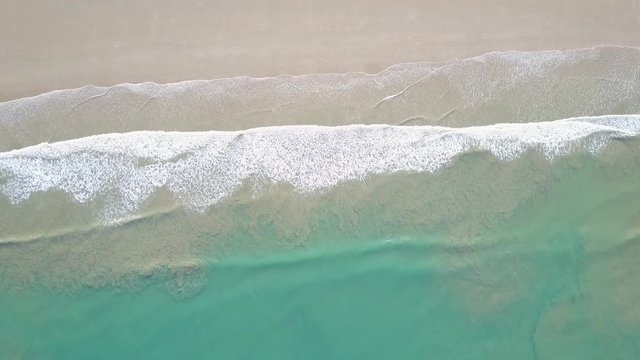 Aerial drone view of waves gently lapping onto sandy sunny beach