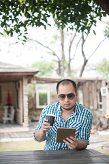 Young man sits outdoors at a wooden table and relaxing with tablet .