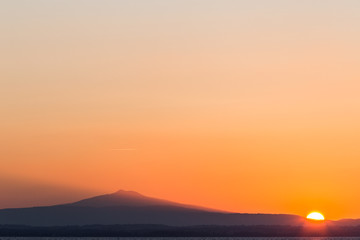 A minimalist sunset, with sun in the lower right angle, projecting light toward a mountain