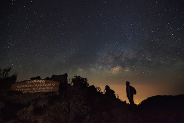 Fototapeta premium Doi Luang Chiang Dao, Chiang Mai - Febuary 13, 2016 : Milky way, Night sky with stars and silhouette of a standing man at Doi Luang Chiang Dao High moutaun top point signs.