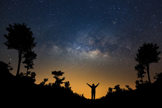 Milky way galaxy and silhouette of a standing happy man in forest, Long exposure photograph, with grain.