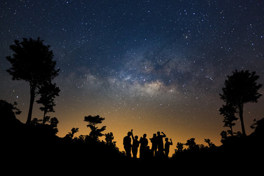 Landscape with milky way, Night sky with stars and silhouette of happy people standing in forest, Long exposure photograph, with grain.