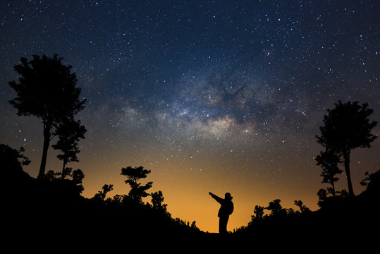 A Man is standing next to the milky way galaxy pointing on a bright star in forest, Long exposure photograph, with grain.