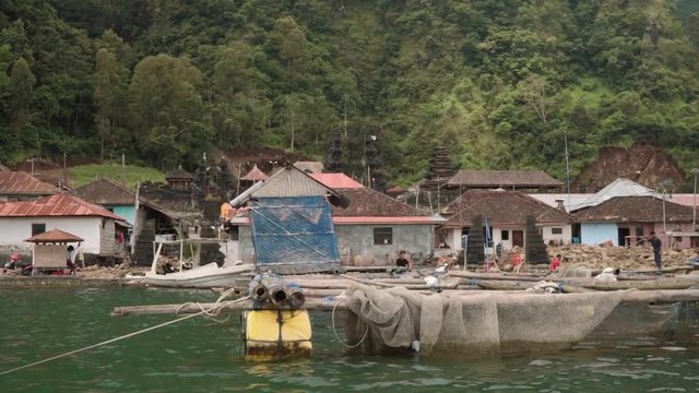 Sailing past traditional Trunyan village on cloudy summer day, view of simple wooden houses, bamboo fish farm and balinese temple from Lake Batur. Shot with Sony a7s in Bali, Indonesia