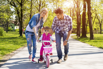 Happy young couple teaching daughter to ride a bicycle on beautiful sunny day