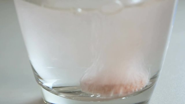 Close-up of an effervescent tablet dissolving in a glass of water, with bubbles rising and creating a fizzy reaction