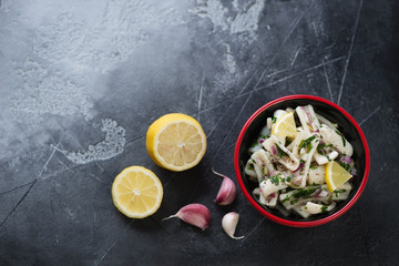 Bowl with calamari salad over dark grey stone background, above view with copyspace, horizontal shot