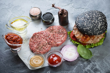 Raw beef cutlets with black burger and cooking ingredients, selective focus
