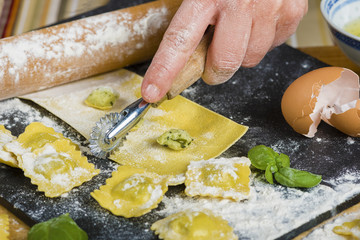 Woman's hand stuffing the dough for making ravioli, in a kitchen with other ingredients and tools...