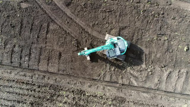 Aerial view moving up hydraulic excavator driving over brown soil flattening sand surface heavy construction vehicle on tracks using hydraulic pumps for movement flock of seagulls searching for food
