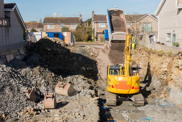 Excavator is digging a house foundation in a residential area while a dumper truck is unloading...