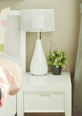 White lamp and flower pot on bedside table next to bed