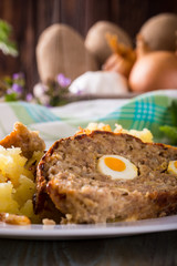 Detail of portion of meatloaf on white plate with mashed potatoes and eggs