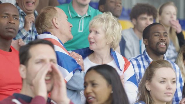  Affectionate mature couple in crowd at sports event draped in British flag